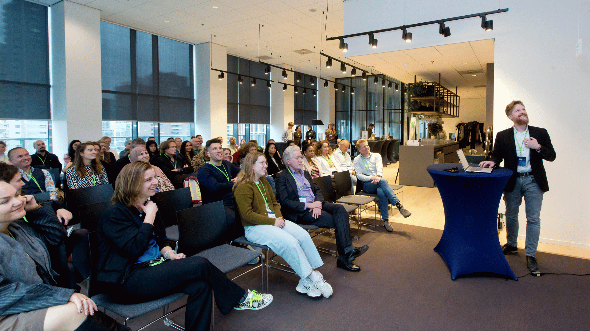 je ziet een zaal met deelnemers en een spreker